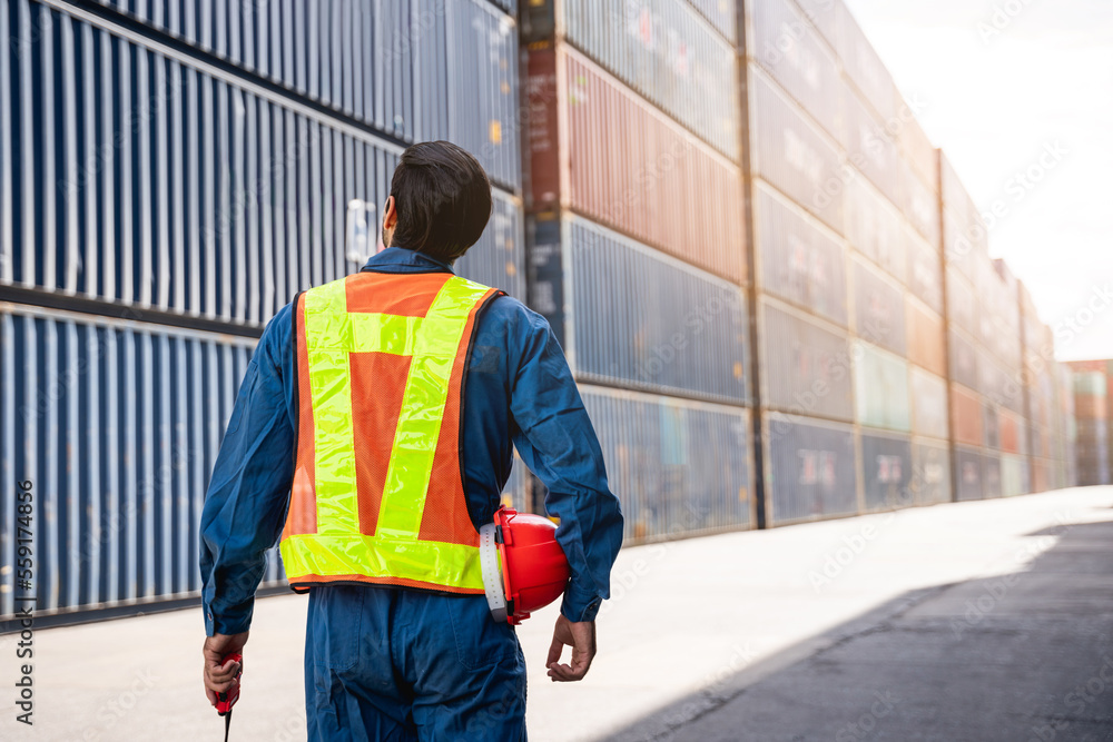 Engineer or foreman standing on the container yard warehouse talk on a portable radio and check inventory or task details., Logistics concept inside the shipping, import, and export industries.