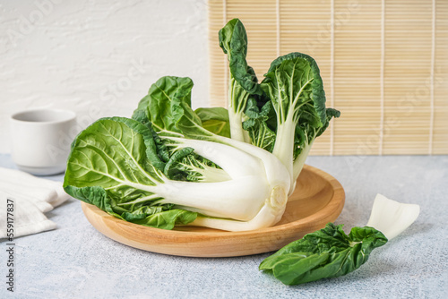 Wooden plate with fresh pak choi cabbage on light background