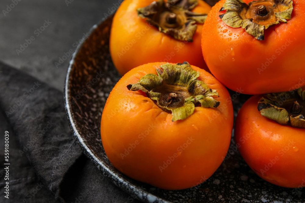 Plate with fresh ripe persimmons on dark background, closeup Plate with fresh ripe persimmons on dark background, closeup