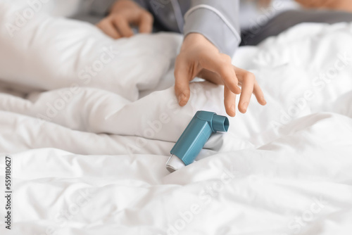 Sick woman with inhaler in bedroom, closeup