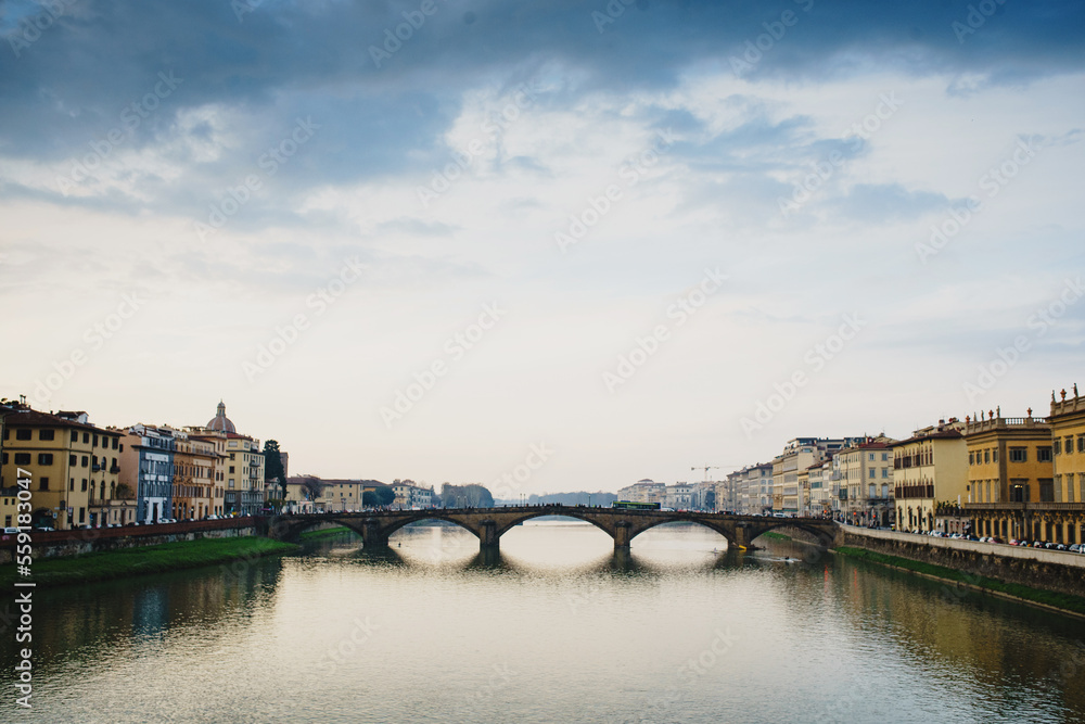 Fototapeta premium Panoramic view of the Ponto Vecchio Bridge and the Arno River in Florence. Reflection in the water of buildings and roofs of houses. Fog, Perspective, typical Tuscan landscape