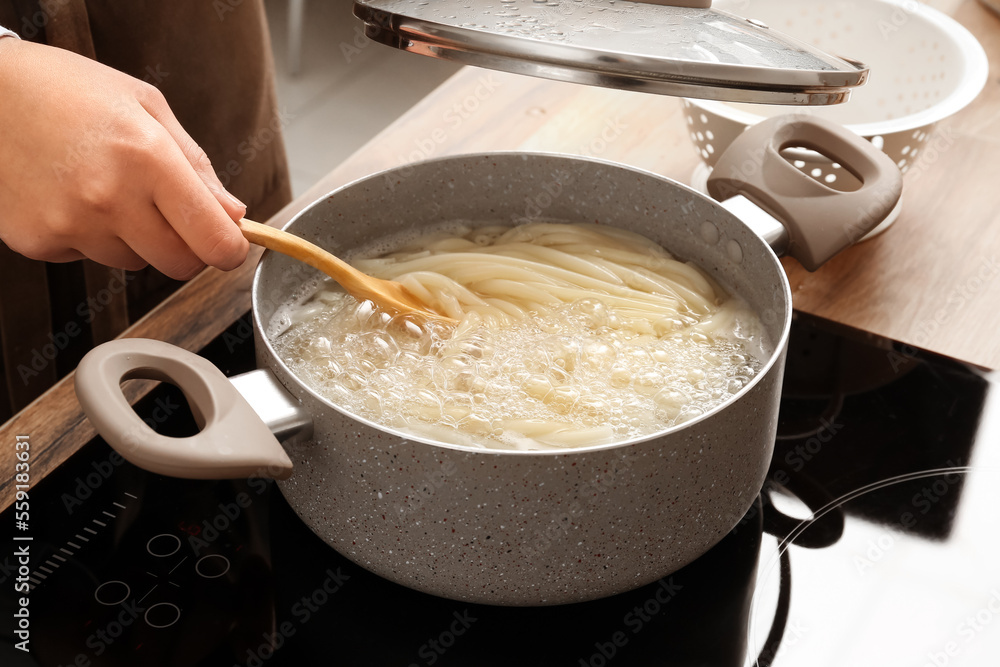Woman preparing delicious pasta on electric stove in kitchen Woman preparing delicious pasta on electric stove in kitchen