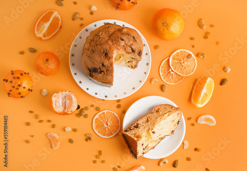 Plates with cut Panettone, citruses, nuts and raisins on orange background