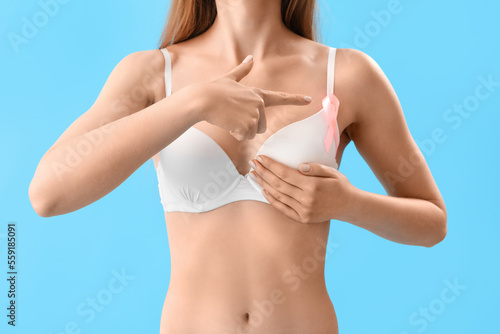 Young woman in underwear pointing at pink ribbon on blue background. Breast cancer awareness concept
