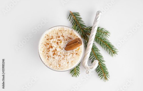 Glass of tasty eggnog cocktail, fir branch and Christmas decoration on white background