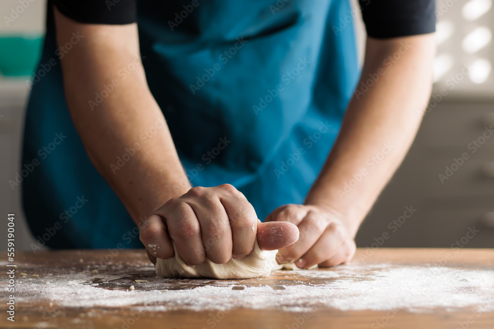 Unrecognizable man kneading by hand on a wooden table in the kitchen of his home Unrecognizable man kneading by hand on a wooden table in the kitchen of his home