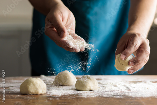 Unrecognizable man kneading dough by hand in the kitchen. Spreading flour on dough balls