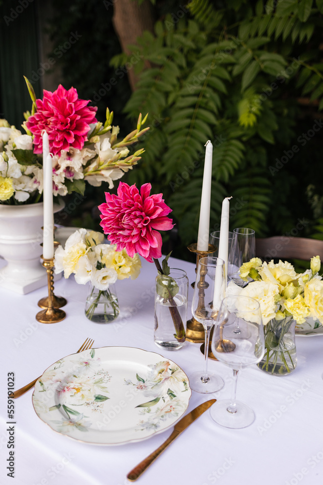 Flowers decorations on the table. Beautiful plates and candles. Table setting by the pink, yellow. white flowers outdoor. Flowers decorations on the table. Beautiful plates and candles. Table setting by the pink, yellow. white flowers outdoor.