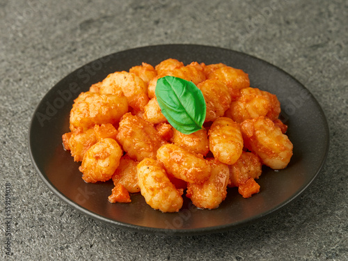 Close-up of a plate of POTATO GNOCCHI with tomato sauce on a gray stone background.