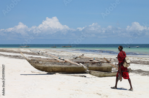 A man in a red near a fishing boat on the shore of ocean