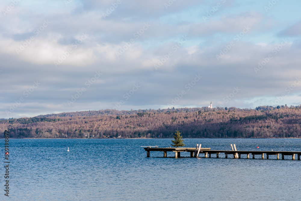 An old wooden footbridge with foliage leads into the Ammersee near Dießen in Bavaria An old wooden footbridge with foliage leads into the Ammersee near Dießen in Bavaria