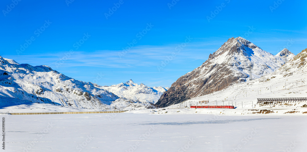 Panorama of the Lake Bianco with the red Rhaetian Rail passing along the lake side and the Alps summit Piz Lagalb at the background Panorama of the Lake Bianco with the red Rhaetian Rail passing along the lake side and the Alps summit Piz Lagalb at the background