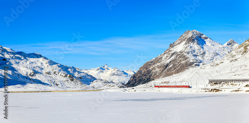 Panorama of the Lake Bianco with the red Rhaetian Rail passing along the lake side  and the Alps summit Piz Lagalb at the background photo