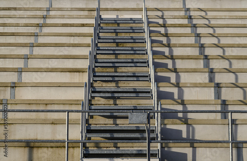 metal stairs in a cement grandstand of a sports center in the french basque country. You can see the stairs that go up on the empty cement stands and the shadow that is projected obliquely on them