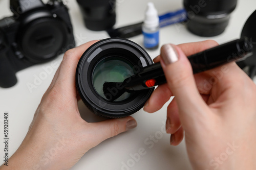 Hands cleaning the lens of a digital camera from dust with a special cleaning brush. The concept of care for photographic equipment, cleaning the camera lens.