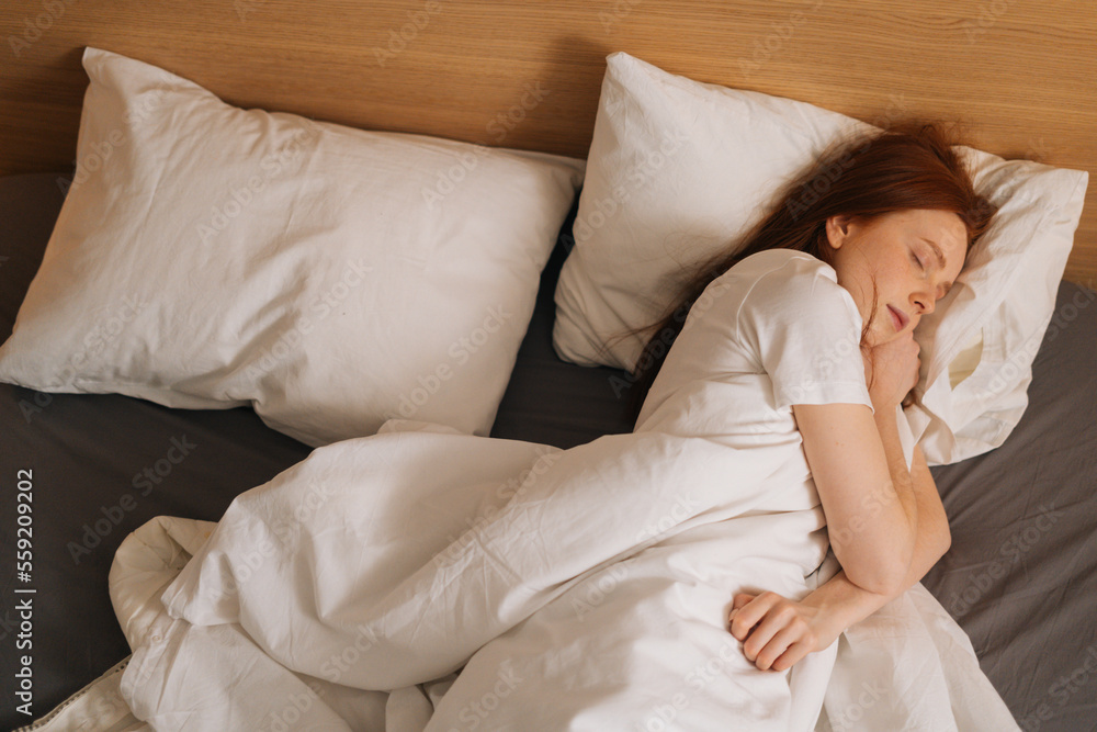 Top view of cute calm redhead young woman wearing soft comfortable night clothes sleeping in comfortable bed lying down on soft pillow. Peaceful pretty lady resting covered with blanket. Top view of cute calm redhead young woman wearing soft comfortable night clothes sleeping in comfortable bed lying down on soft pillow. Peaceful pretty lady resting covered with blanket.
