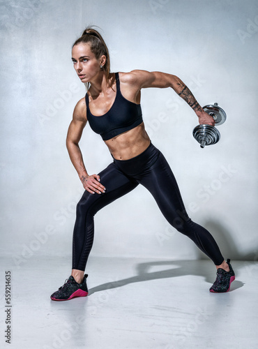 Sporty woman working out with dumbbells. Photo of model in black sportswear on grey background. Sports motivation and healthy lifestyle