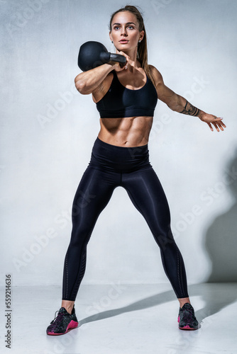 Sporty woman workout with kettlebell. Photo of woman in black sportswear on grey background. Sports motivation and healthy lifestyle © Romario Ien