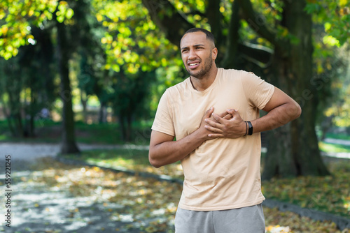 Fototapeta Naklejka Na Ścianę i Meble -  Hispanic athlete in the park has severe chest pain, man has a heart attack while jogging and doing fitness and exercise in the park outdoors.
