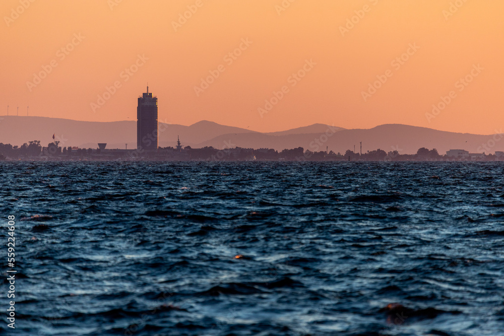 Tower behind the sea bay in sunset light with mountains and orange sky behind