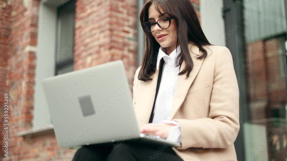 Charming young businesswoman working on laptop sitting on stairs in the urban brick space Busy woman have distance freelance work on computer outdoors Charming young businesswoman working on laptop sitting on stairs in the urban brick space Busy woman have distance freelance work on computer outdoors