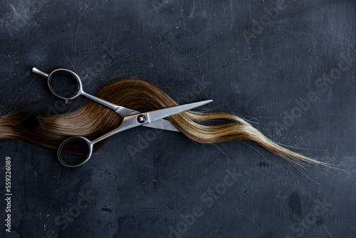 Fotografija scissors with a lock of hair on a gray textured background, hair cutting, space