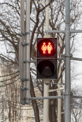 A red traffic light with the image of two female figures with hearts on a pedestrian crossing, prohibiting the signal light.