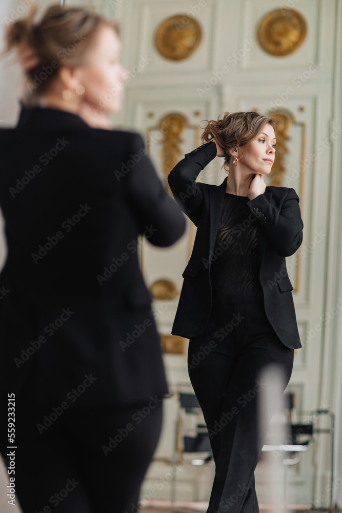 an attractive sexy woman in a black suit looks at her reflection in the mirror an attractive sexy woman in a black suit looks at her reflection in the mirror