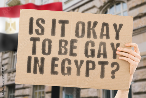 The question " Is it okay to be gay in Egypt? " is on a banner in men's hands with blurred background. Friendly. Passionate. Contact. Date. Dating. Lover. Partner. Boyfriend. Pleasant. Approval