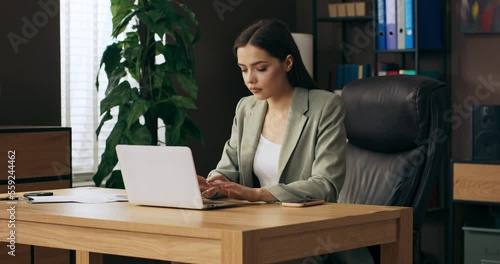 Woman in buisness suit sitting at chair works online from home feels relieved and motivated relaxes after hard work holds phoe in hand and legs on desk . photo