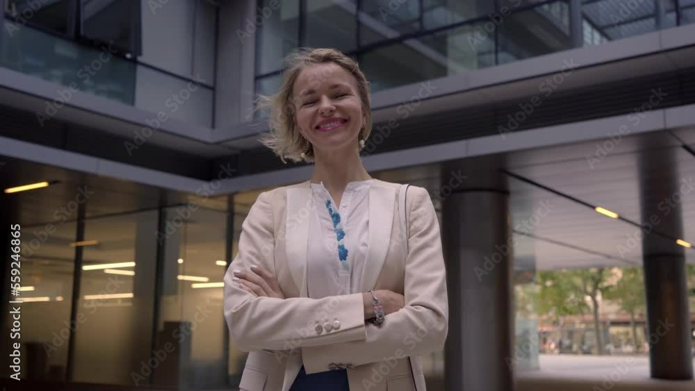 Charming portrait of mature businesswoman looking at camera smiling and crossing arms while standing outside financial building. Charming portrait of mature businesswoman looking at camera smiling and crossing arms while standing outside financial building.