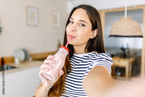 Joyful young adult woman taking selfie portrait while drinking fresh fruit healthy milk shake