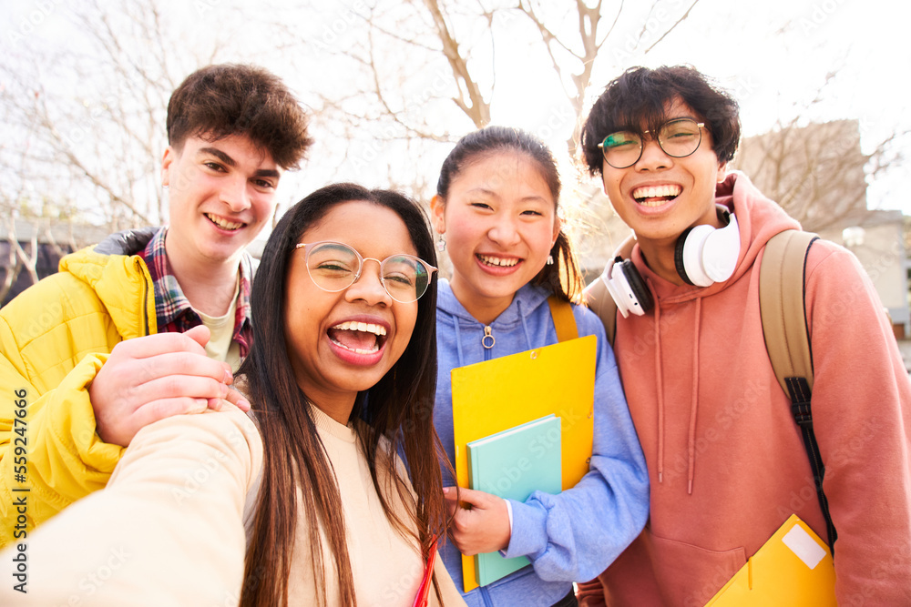 Obraz premium Selfie of Four international students with beaming smiles are posing for photo shot, latin attractive lady is taking, in school library and folder. Gathered, cheerful, smart and successful youth
