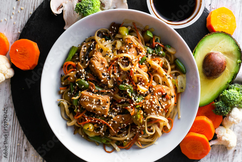 Wok, noodles, udon with chicken, on black plate and a wooden white background top view