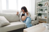 Pregnant woman smile blogger takes vitamins and medicines sitting on the couch at home freelancer in the last month of pregnancy lifestyle before childbirth