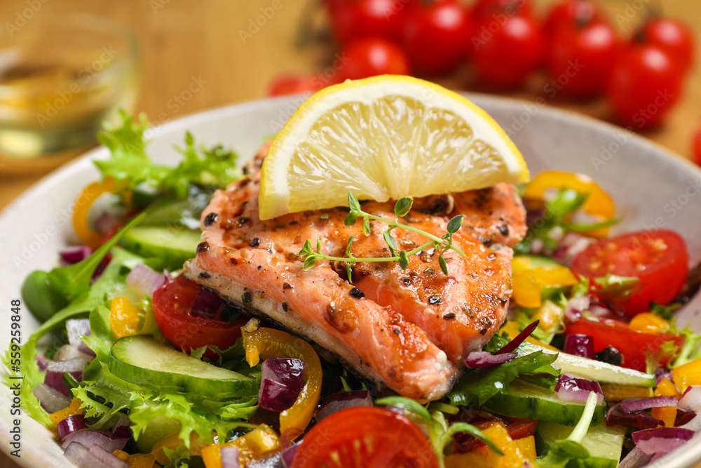 Bowl with tasty salmon, lemon and mixed vegetables on table, closeup