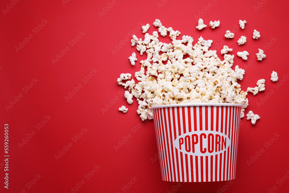 Overturned paper bucket with delicious popcorn on red background, flat lay. Space for text