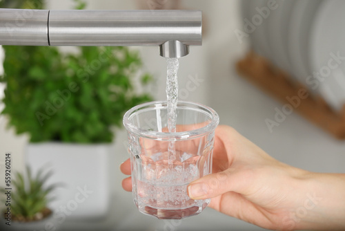 Woman filling glass with tap water from faucet in kitchen, closeup