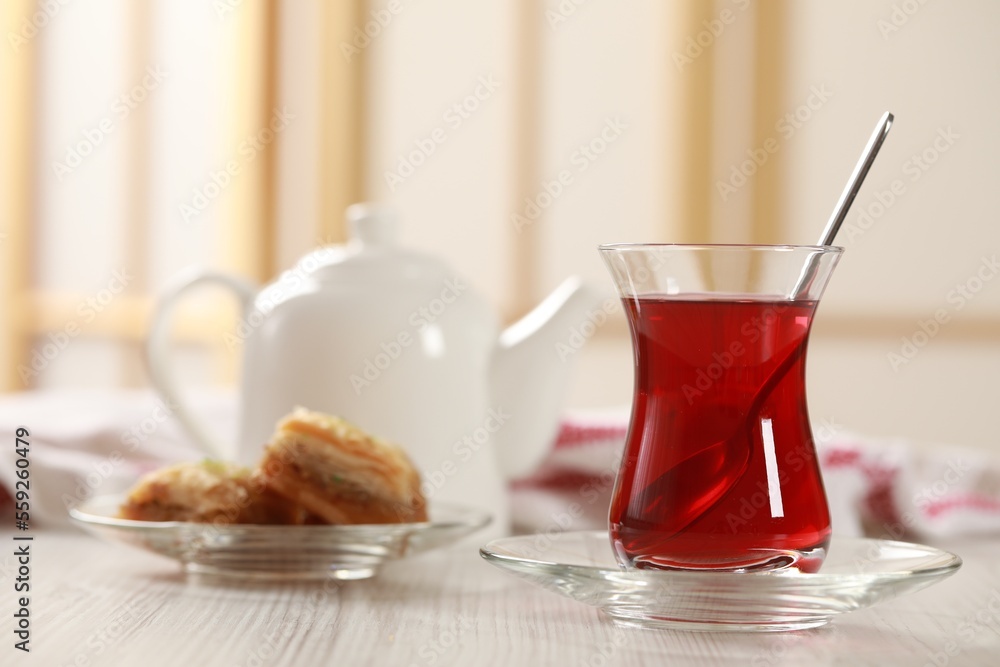 Glass of traditional Turkish tea and sweet baklava on white wooden table indoors. Space for text Glass of traditional Turkish tea and sweet baklava on white wooden table indoors. Space for text