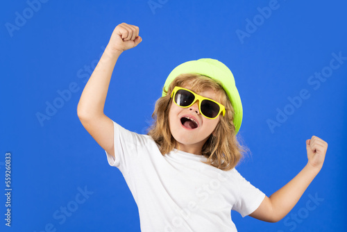 Fashion portrait of kid in summer hat, t-shirt and sunglasses on blue studio isolated background. Excited kid boy on studio isolated background. Surprised face, amazed emotions of child.