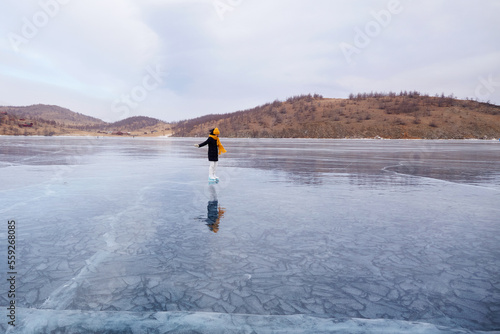 A young athletic girl is skating on the transparent ice of the frozen Lake Baikal. Active winter holidays.
