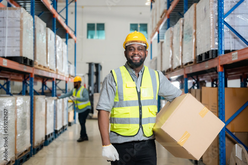 Smiling African male warehouse worker leaning against some boxes.