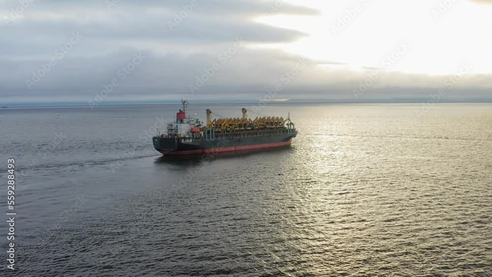 Aerial: Cargo ship in motion with construction equipment on deck Aerial: Cargo ship in motion with construction equipment on deck
