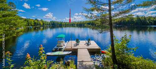 Two Ontario chairs sitting on a wood dock facing a calm lake. photo