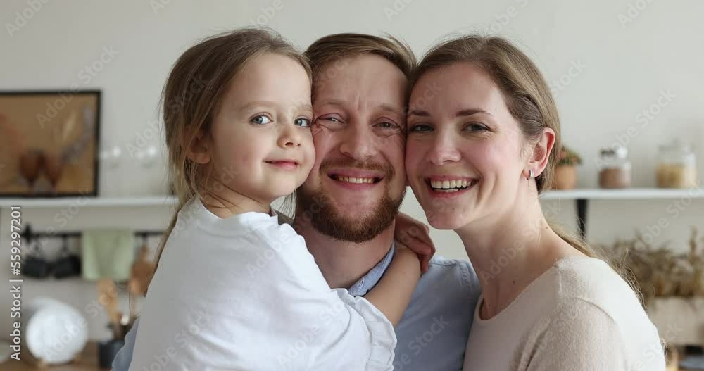 Close up portrait happy family with little daughter. Young loving parents cuddling cute preschooler kid girl smile looking at camera feeling unconditional love, spend time together standing in kitchen Close up portrait happy family with little daughter. Young loving parents cuddling cute preschooler kid girl smile looking at camera feeling unconditional love, spend time together standing in kitchen
