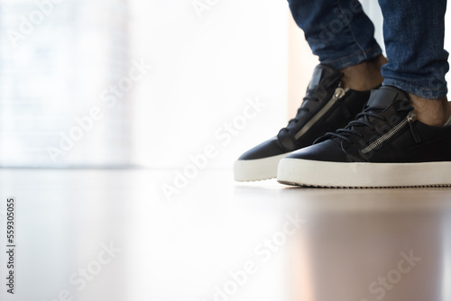 Feet in stylish sneakers of unknown African man standing or walking on clean laminate floor inside modern hotel, house or apartment, close up shot. Floor repair and installation services advertisement