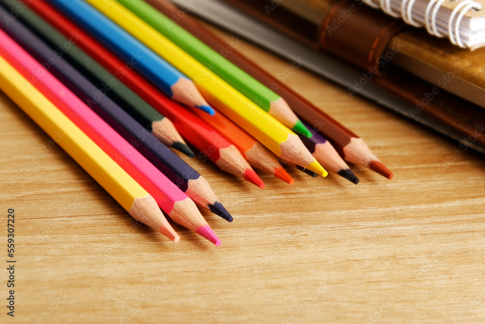 colored pencils against the background of a desk, notebook, white wall colored pencils against the background of a desk, notebook, white wall
