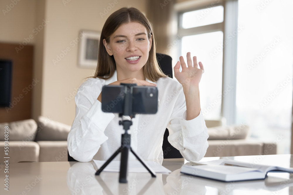 Attractive woman greets followers sit at desk staring at cellphone screen start streaming, making video call by study, filming job interview. Modern tech usage for distancing communication, vlogging Attractive woman greets followers sit at desk staring at cellphone screen start streaming, making video call by study, filming job interview. Modern tech usage for distancing communication, vlogging