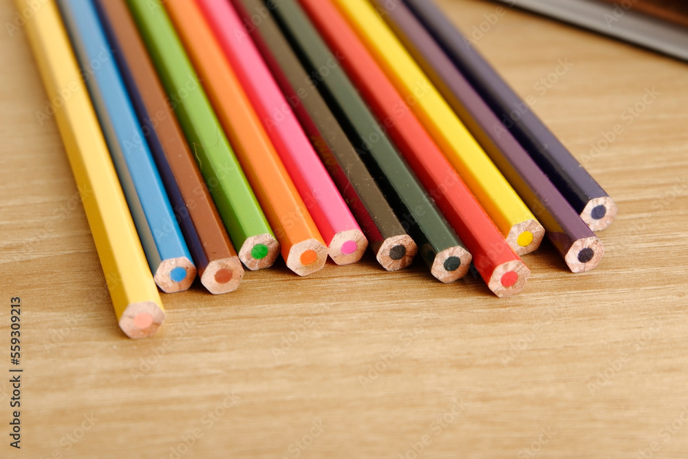 Fototapeta premium colored pencils against the background of a desk, notebook, white wall