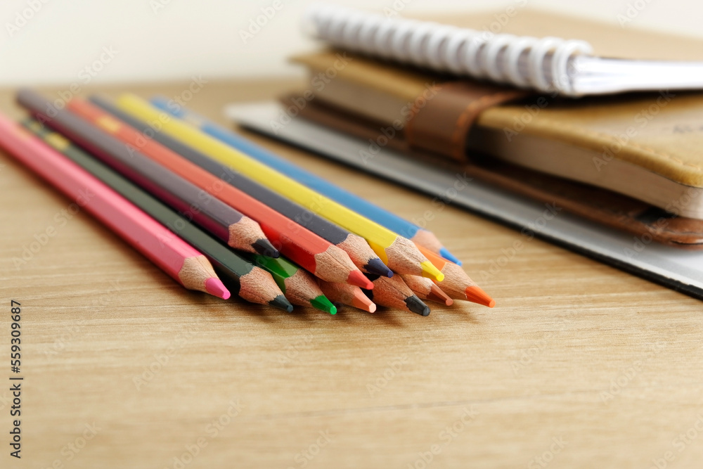colored pencils against the background of a desk, notebook, white wall colored pencils against the background of a desk, notebook, white wall